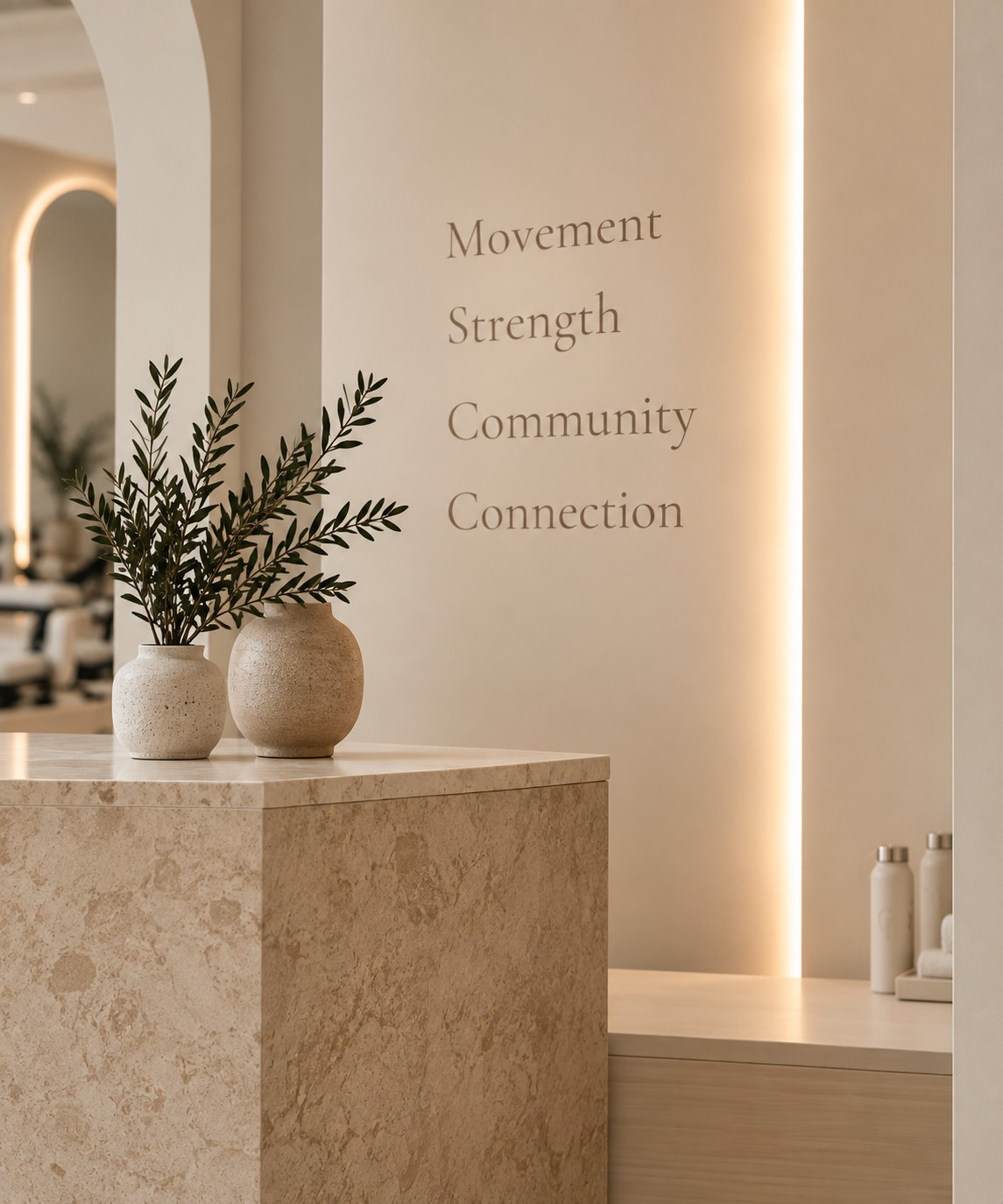 Travertine reception desk with olive branches in ceramic vases beside a wall reading Movement, Strength, Community, Connection